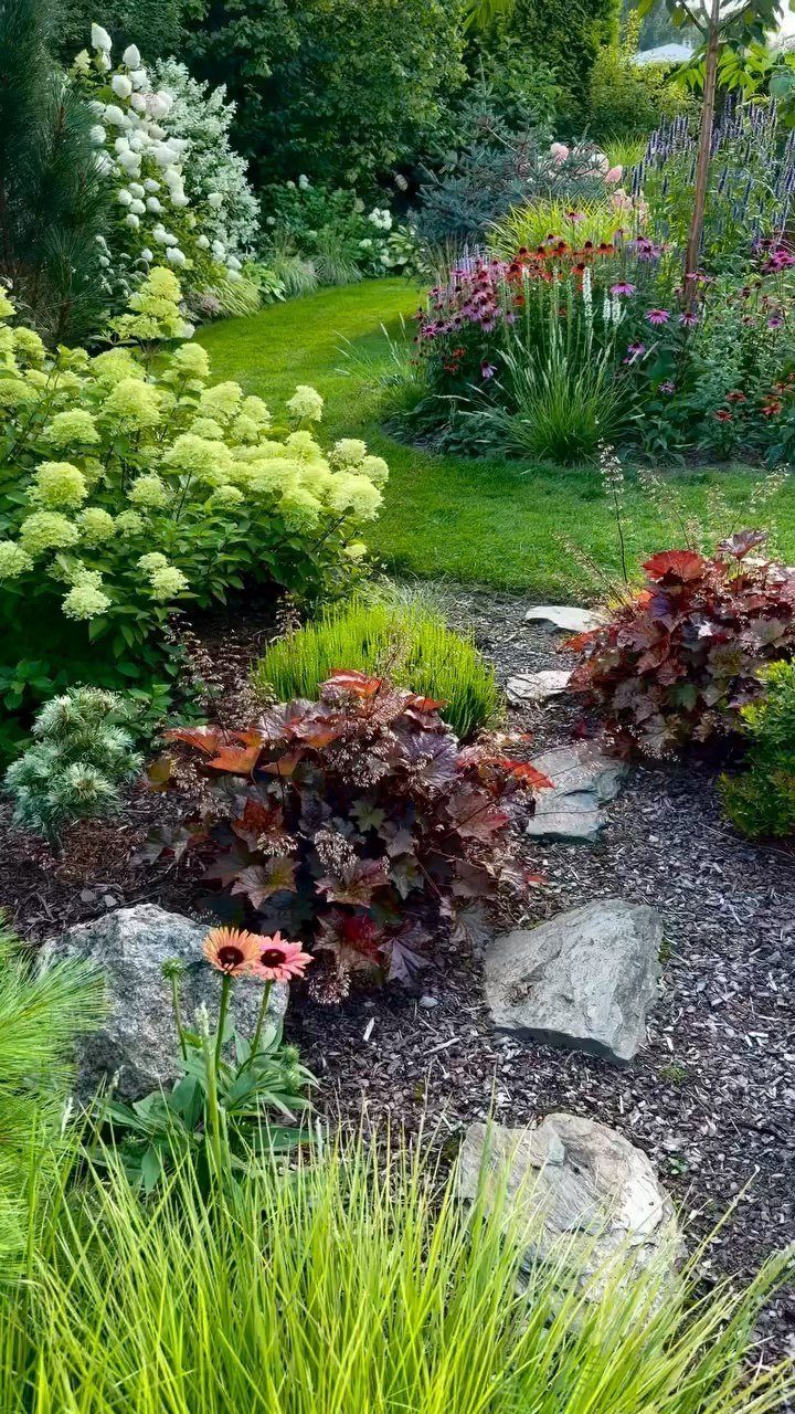 15 Acreage Garden Ideas for Large Land That Works 14 Lush garden landscape with green grass, colorful flowering shrubs, and dark-leaved perennials in mulch.
