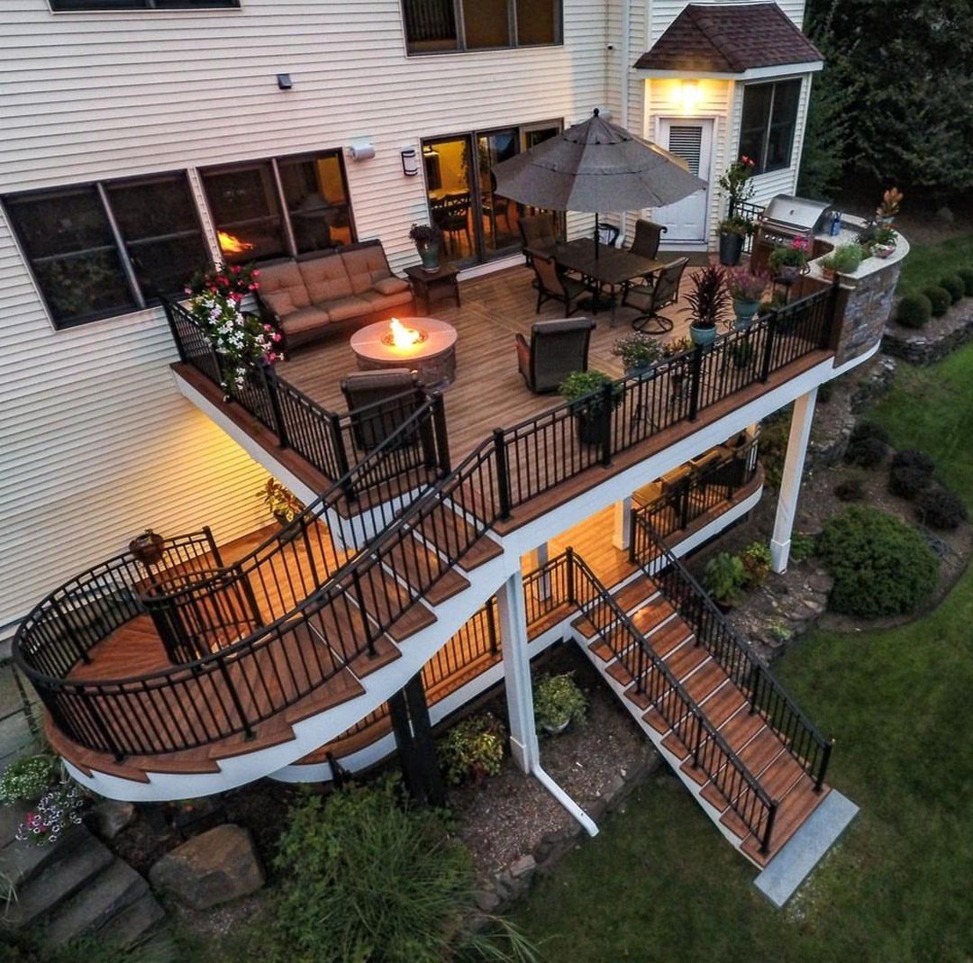 15 Acreage Garden Ideas for Large Land That Works 12 A large multi-level wooden deck with black railings, outdoor furniture, and a fire pit attached to a house.