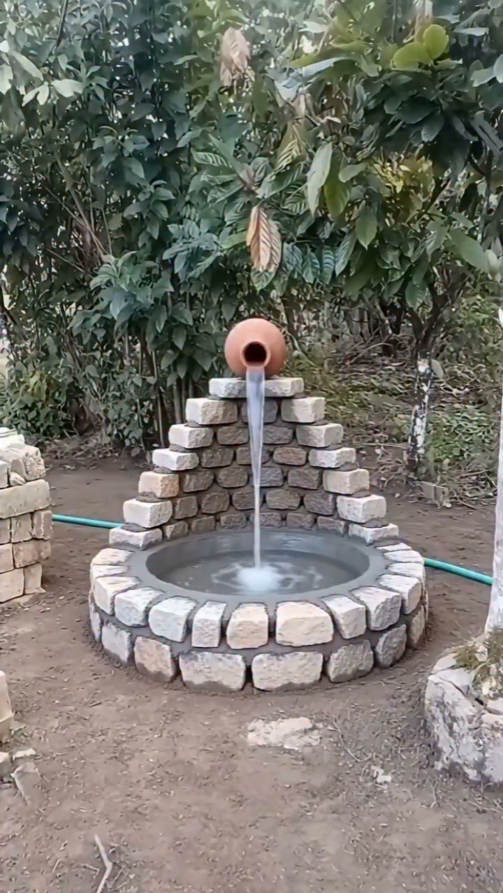 15 Acreage Garden Ideas for Large Land That Works 5 A terracotta pot pouring water into a circular stone basin surrounded by a small brick pyramid.