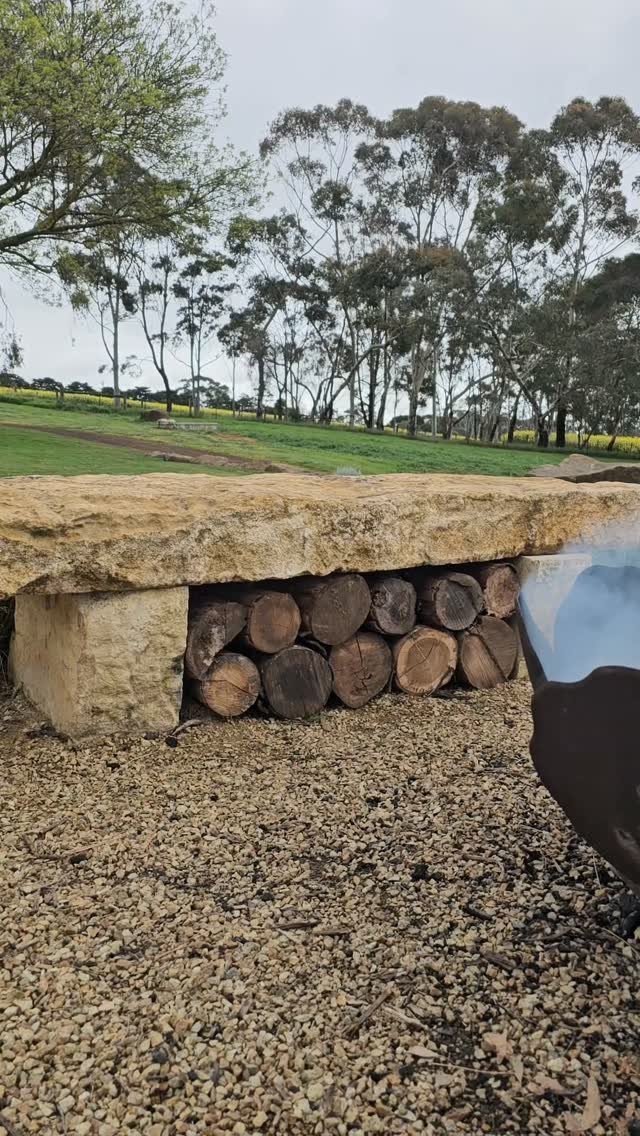 21 Back Garden Ideas from Potagers to Fire Pits 9 Stone bench with stacked logs stored underneath on a gravel ground.