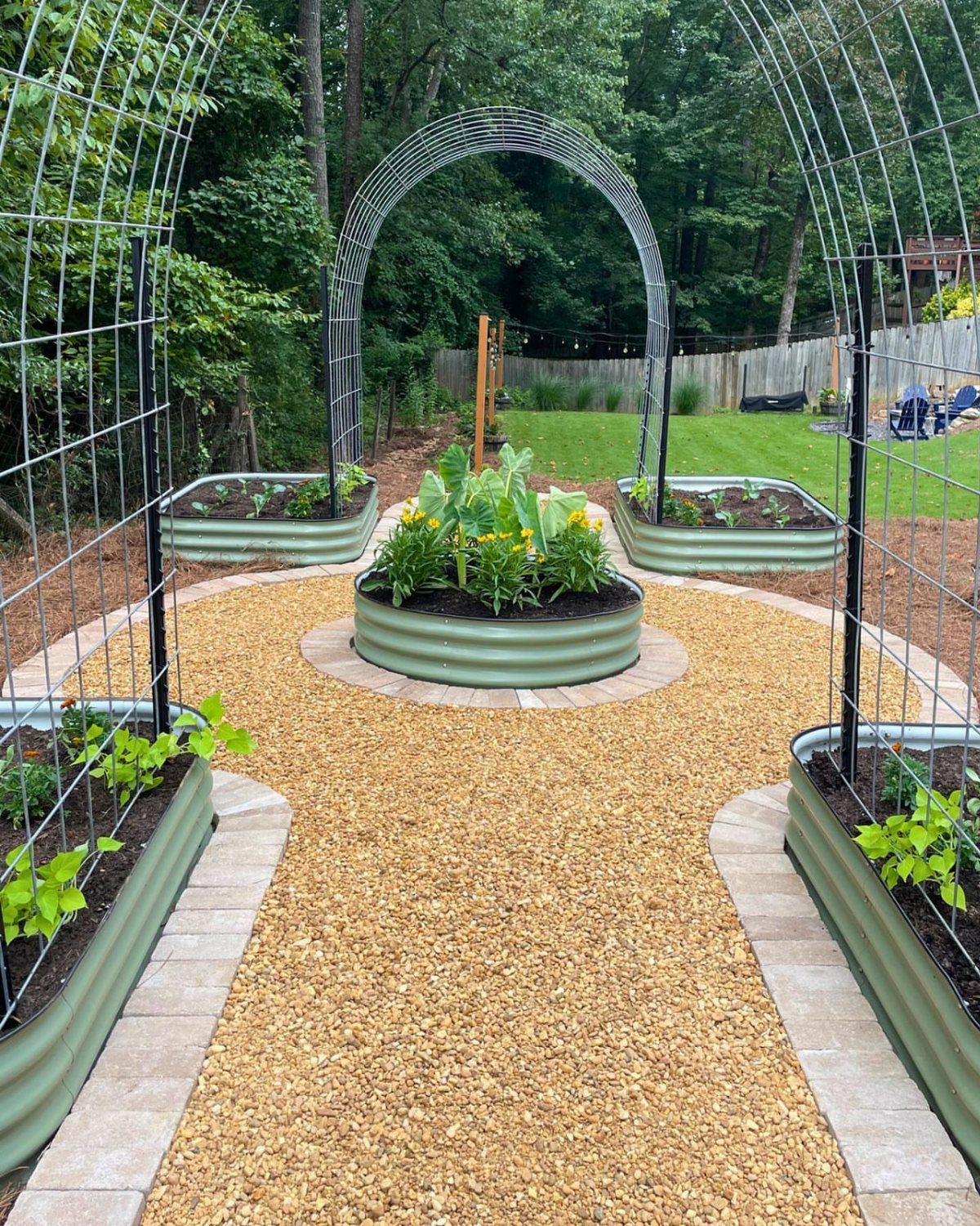 21 Back Garden Ideas from Potagers to Fire Pits 14 Metal arched trellises over gravel paths and corrugated metal raised garden beds in a backyard.