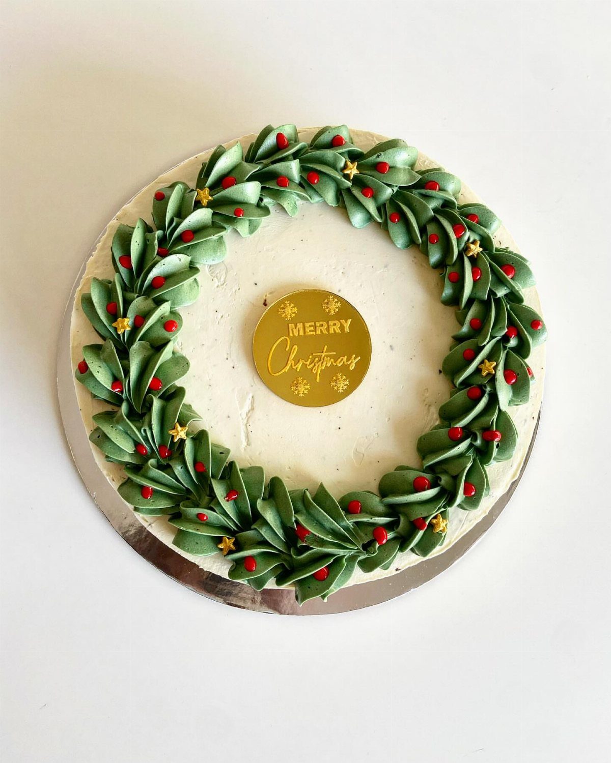 12 Beautiful Christmas Cake Ideas That Rival Bakery Work 8 A white frosted cake decorated with a green buttercream wreath and a gold Merry Christmas tag.
