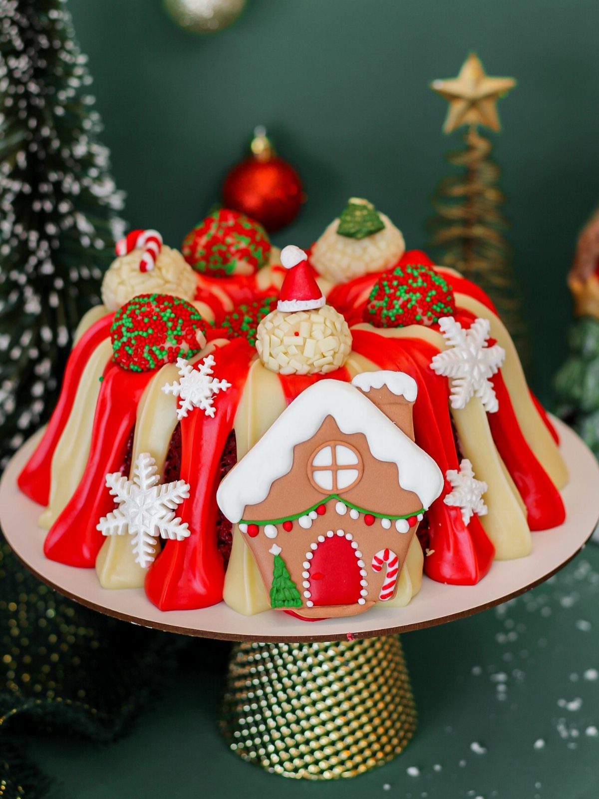 12 Beautiful Christmas Cake Ideas That Rival Bakery Work 12 A decorated bundt cake with red and white icing, snowflakes, and a gingerbread house decoration.