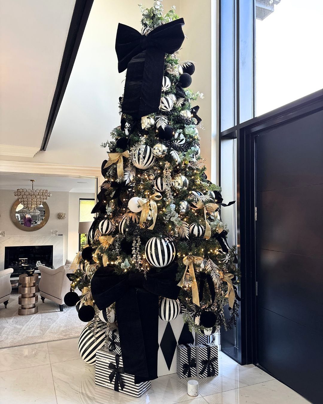 14 Beautiful Christmas Tree Decorations and How to Style Them 12 Decorated Christmas tree with black and white ornaments, large black bows, and gold ribbons in a modern room.