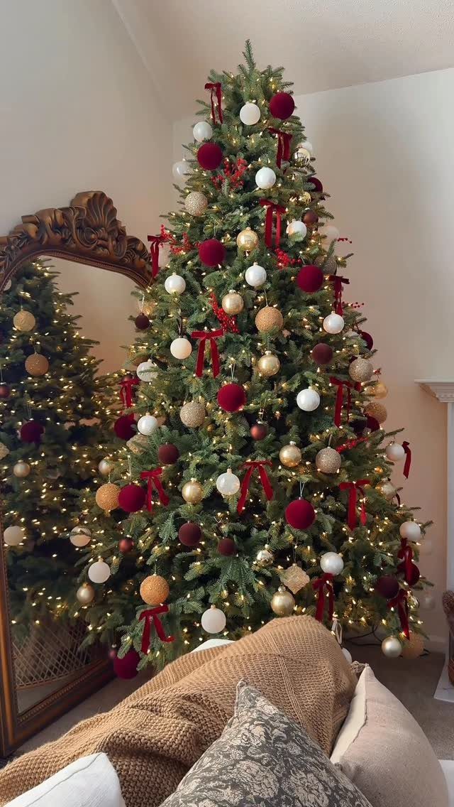 14 Beautiful Christmas Tree Decorations and How to Style Them 10 Decorated Christmas tree with red, gold, and white ornaments and warm lights next to a mirror.