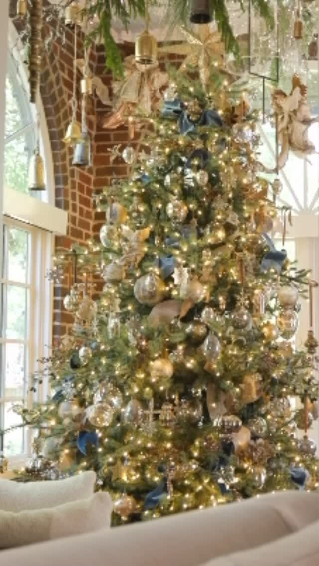 14 Beautiful Christmas Tree Decorations and How to Style Them 8 A large Christmas tree decorated with gold ornaments, blue ribbons, and glowing warm lights.