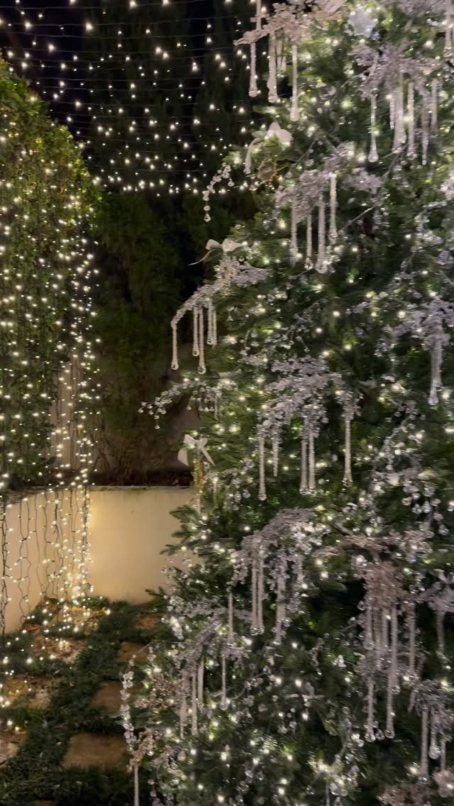 14 Beautiful Christmas Tree Decorations and How to Style Them 2 Decorated Christmas tree with silver icicle ornaments and white lights under hanging string lights.