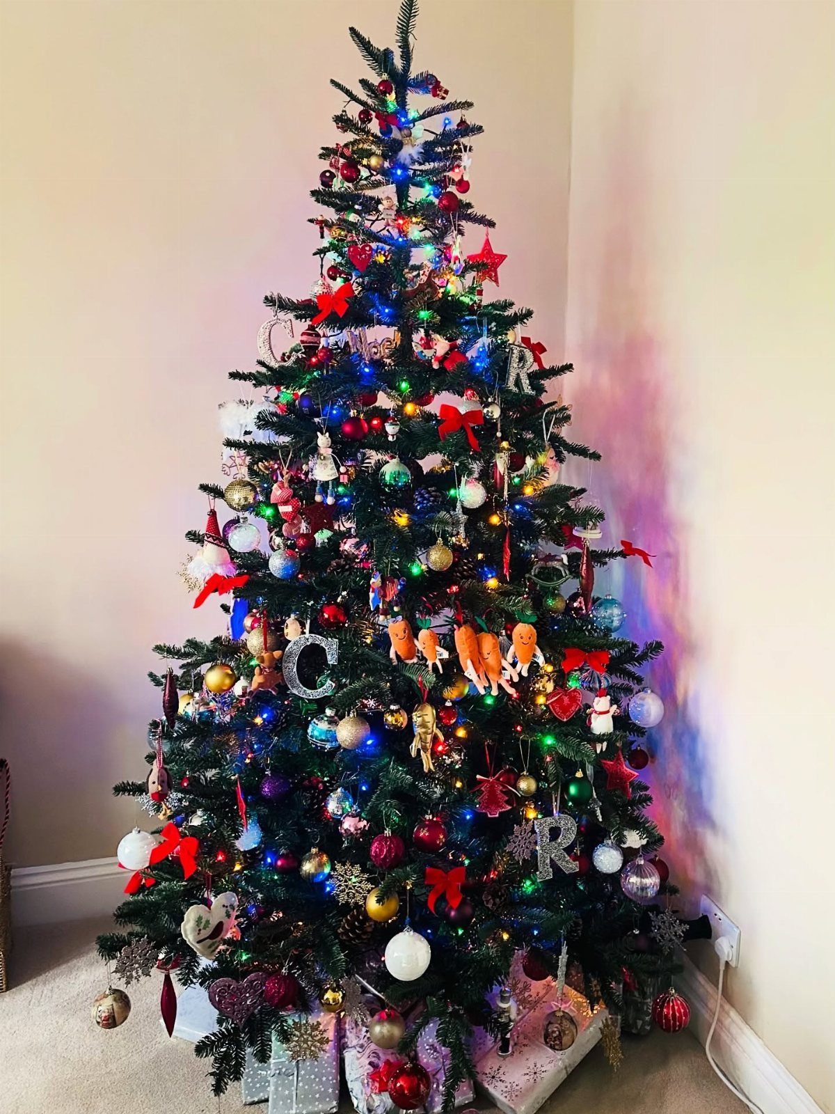 14 Beautiful Christmas Tree Decorations and How to Style Them 13 A decorated Christmas tree with colorful lights, red bows, and various ornaments standing in a room corner.