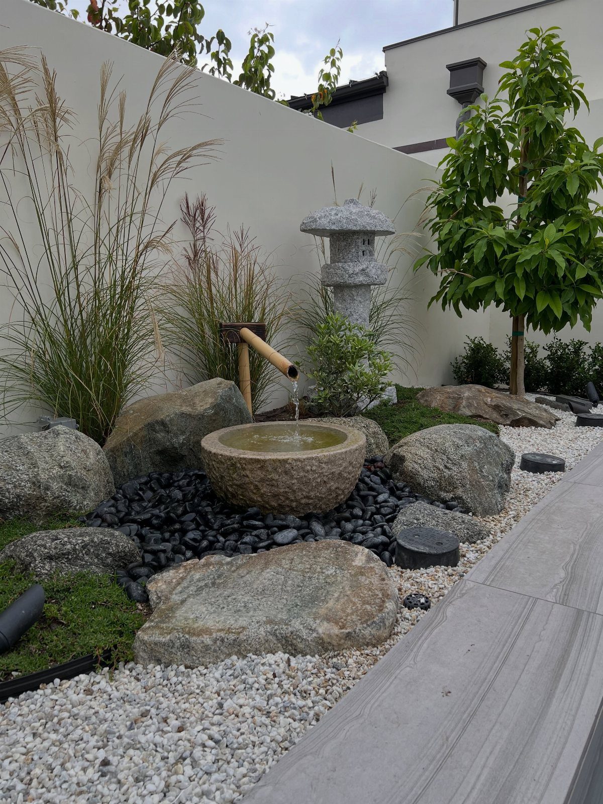 17 Cheap Yard Ideas for a Better Front or Back Garden 2 A stone water basin with a bamboo spout surrounded by rocks and gravel in a Zen garden.