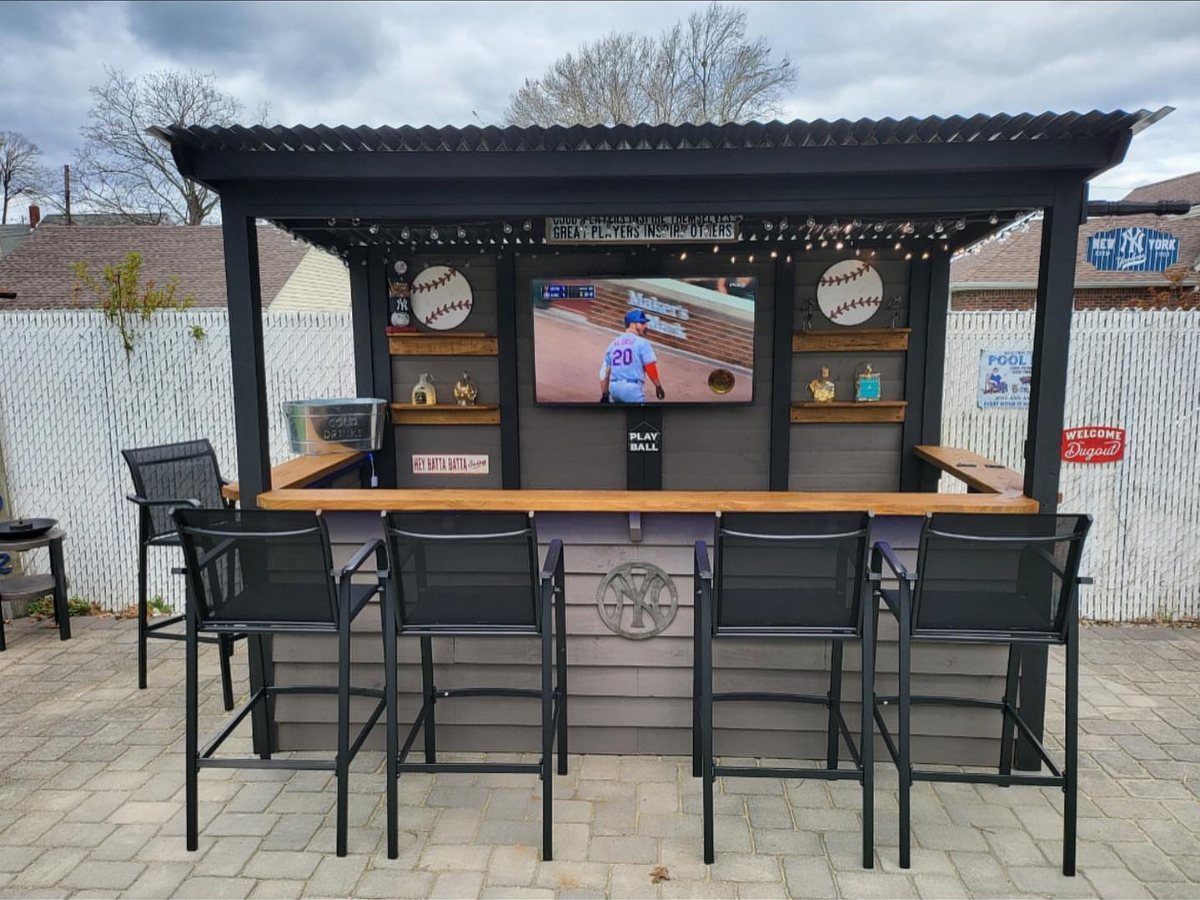 17 Cheap Yard Ideas for a Better Front or Back Garden 15 A black outdoor bar with a wooden counter, television, and black bar stools on a patio.