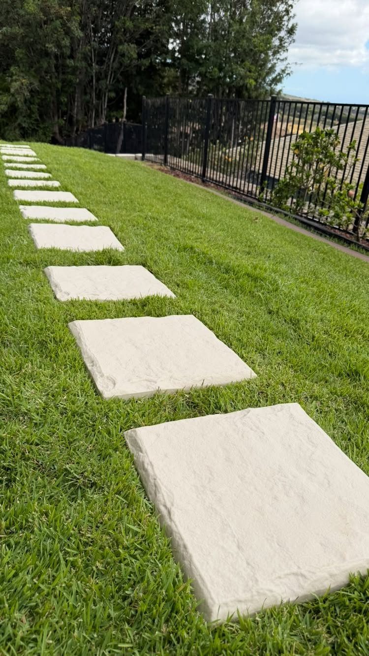 17 Cheap Yard Ideas for a Better Front or Back Garden 9 Rectangular light stone pavers forming a path through a green grass lawn next to a fence.