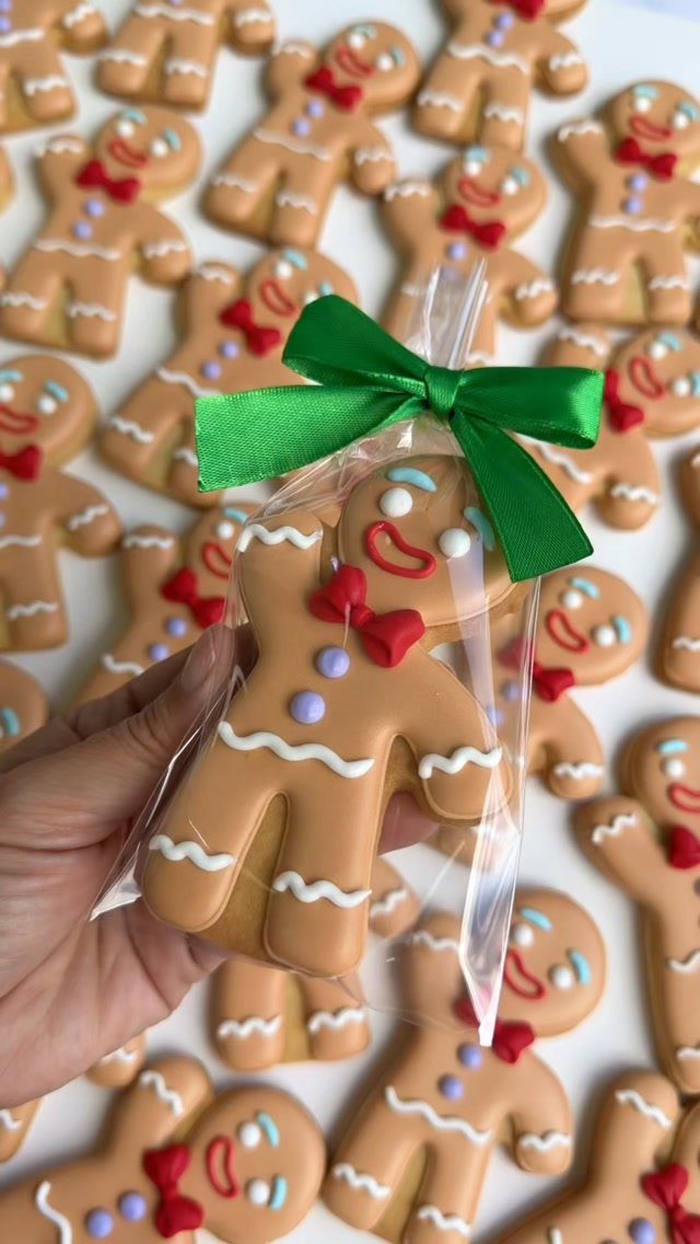 13 Christmas Cookie Decorations Ideas for Your Holiday Baking 10 A hand holding a packaged gingerbread man cookie decorated with white icing and a red bow.