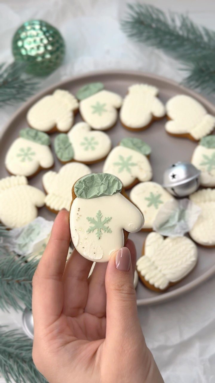 13 Christmas Cookie Decorations Ideas for Your Holiday Baking 9 A hand holding a white iced mitten cookie with a green snowflake design.