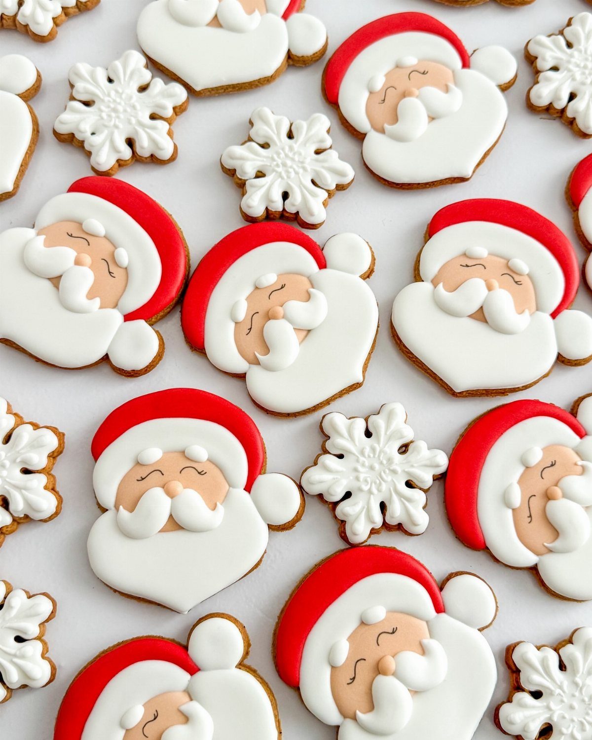 13 Christmas Cookie Decorations Ideas for Your Holiday Baking 5 Santa Claus face cookies and white snowflake cookies scattered on a white surface.
