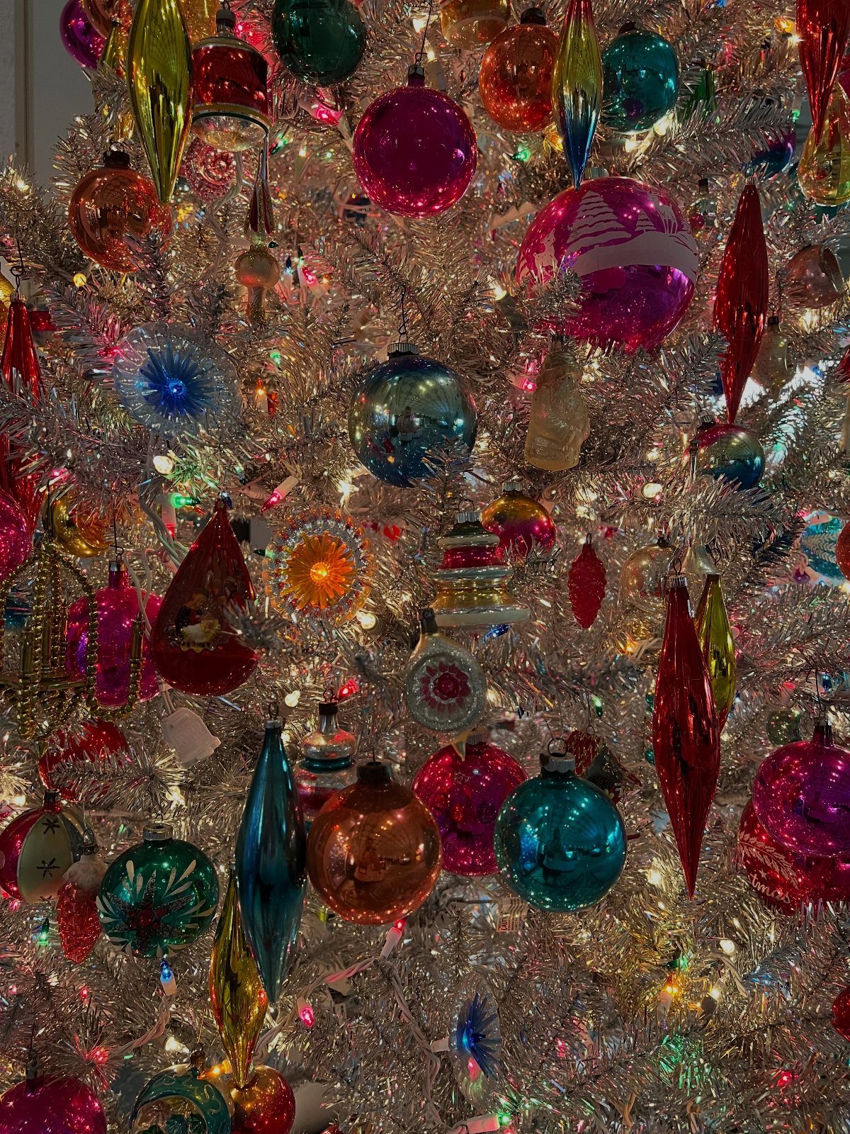 Christmas Decor Aesthetic: 13 Looks to Try This Season 3 Colorful vintage glass ornaments hanging on a shimmering silver tinsel Christmas tree.