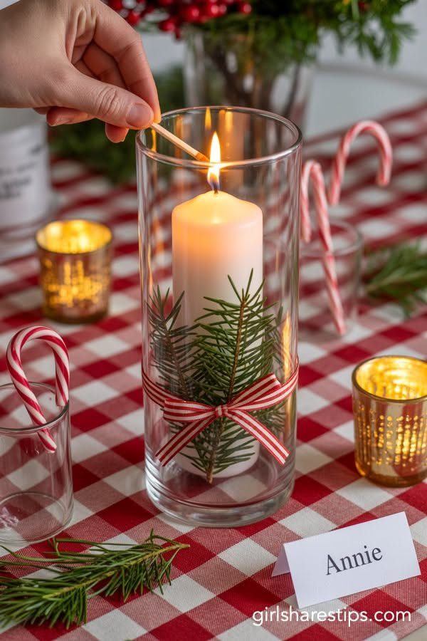 Christmas Dinner and Table Decorations: 9 Ideas for Setting the Scene 1 A hand lights a white pillar candle decorated with greenery inside a glass cylinder on a checkered tablecloth.