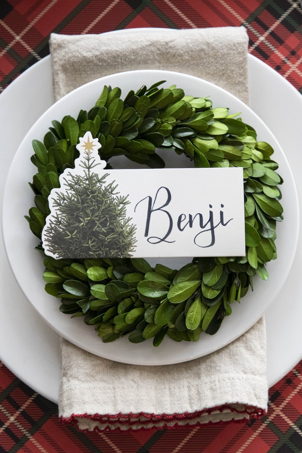 Christmas Dinner and Table Decorations: 9 Ideas for Setting the Scene 7 A green leaf wreath on a white plate featuring a name tag with a tree illustration.