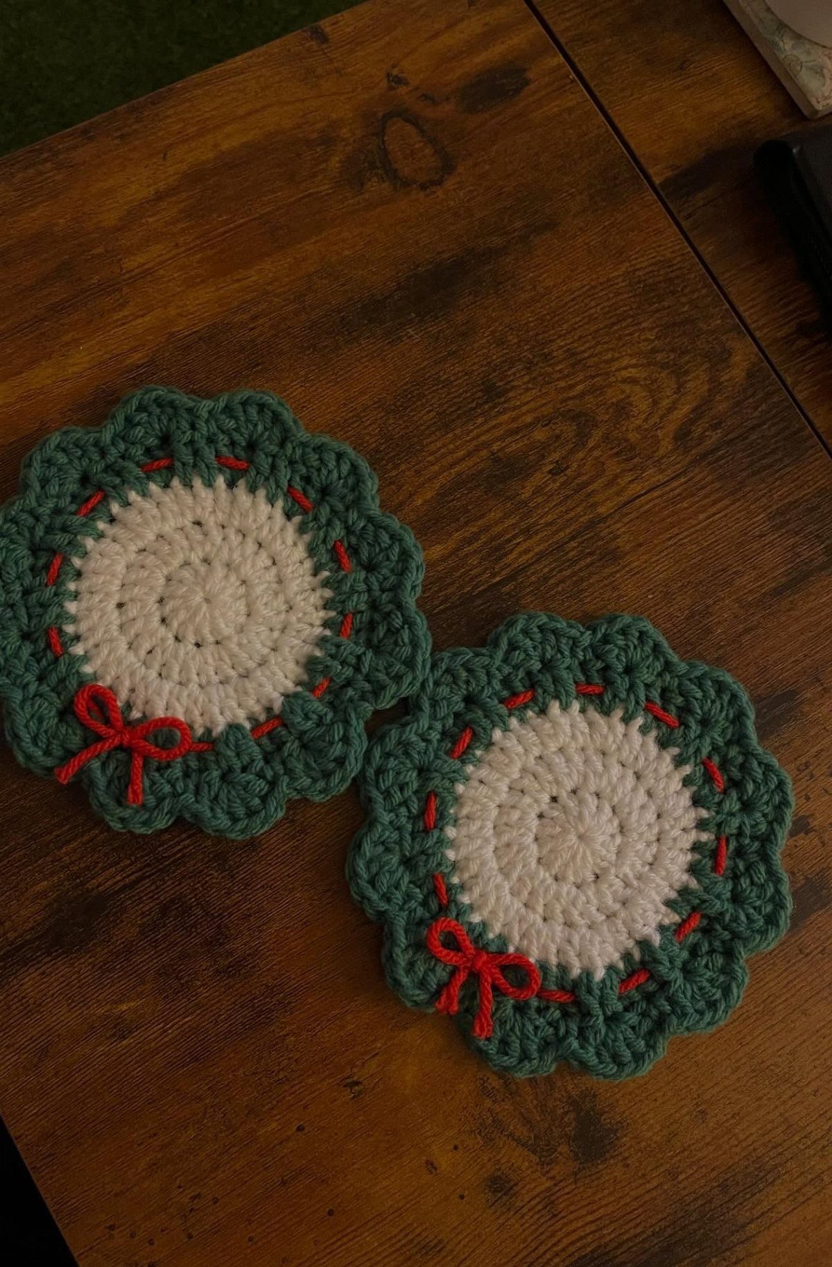 18 Christmas Gift Crochet Ideas for Everyone on Your List 12 Two green and white crochet coasters with red bows sitting on a wooden table.