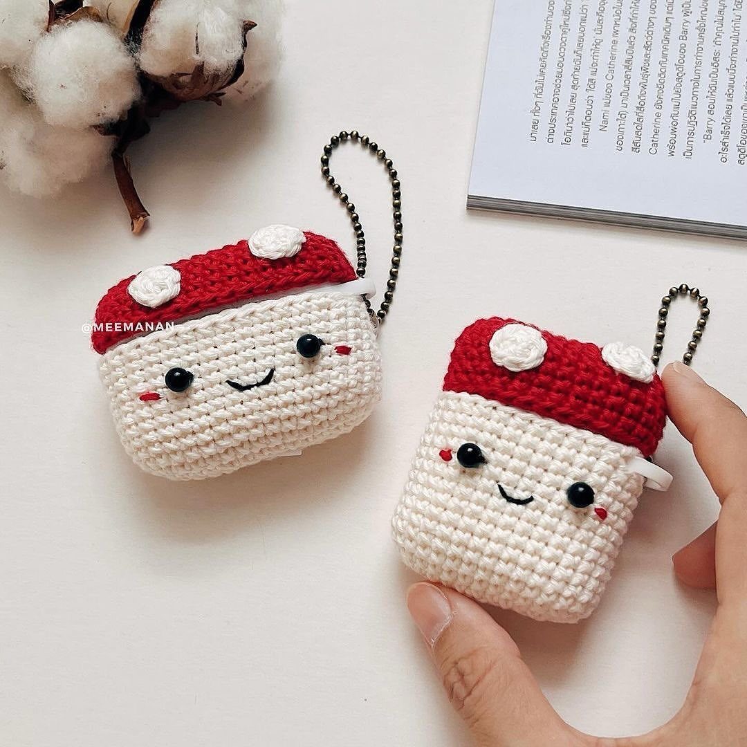 18 Christmas Gift Crochet Ideas for Everyone on Your List 11 Two mushroom-shaped crochet earbud cases with smiling faces on a white surface.