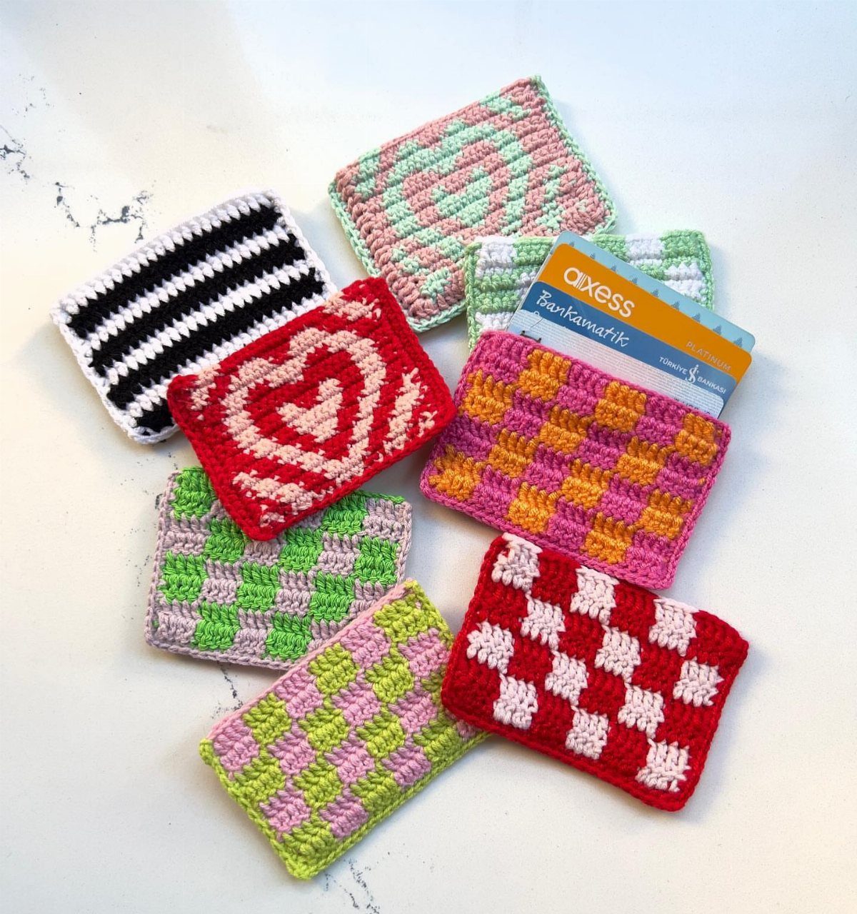 18 Christmas Gift Crochet Ideas for Everyone on Your List 6 Various colorful patterned crochet pouches scattered on a white surface, one holding a blue bank card.