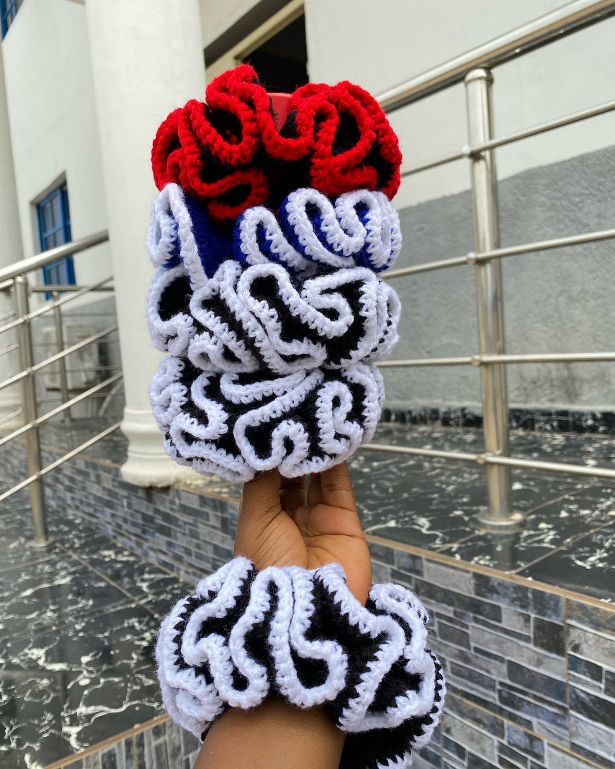 18 Christmas Gift Crochet Ideas for Everyone on Your List 18 Hand holding several colorful crochet hair scrunchies against a tiled outdoor background.