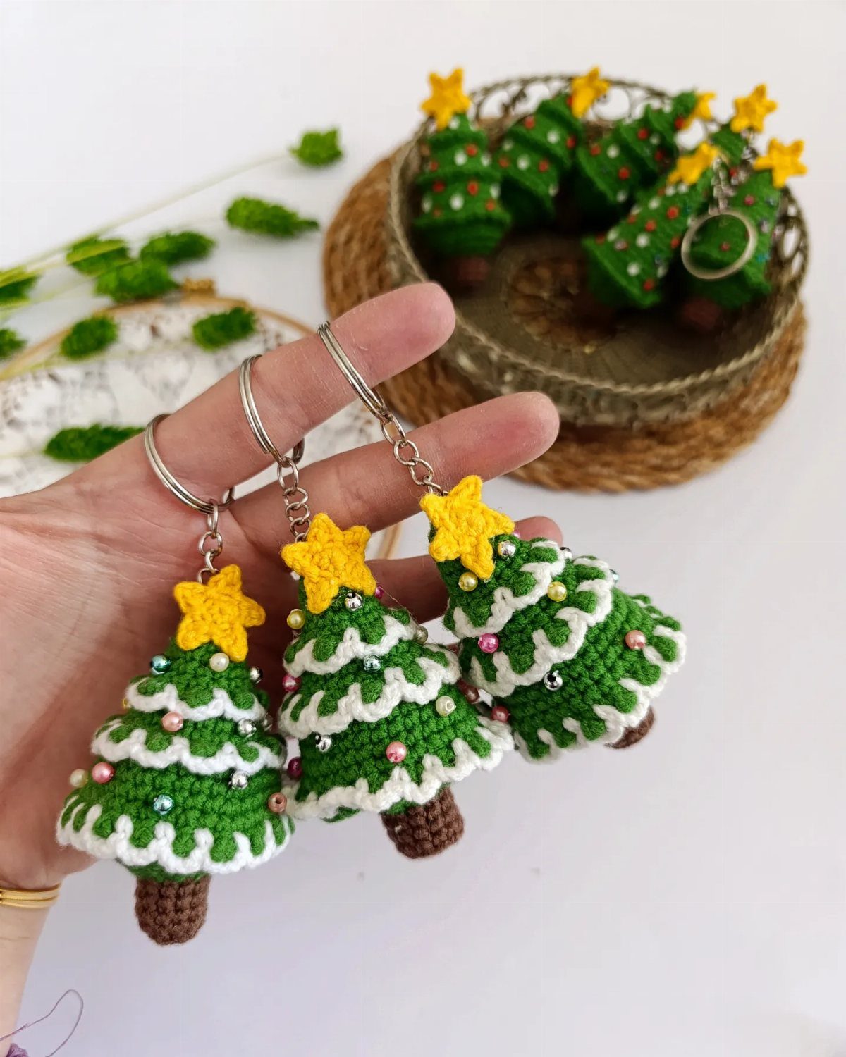18 Christmas Gift Crochet Ideas for Everyone on Your List 14 A hand holding three small crocheted Christmas tree keychains with yellow stars.