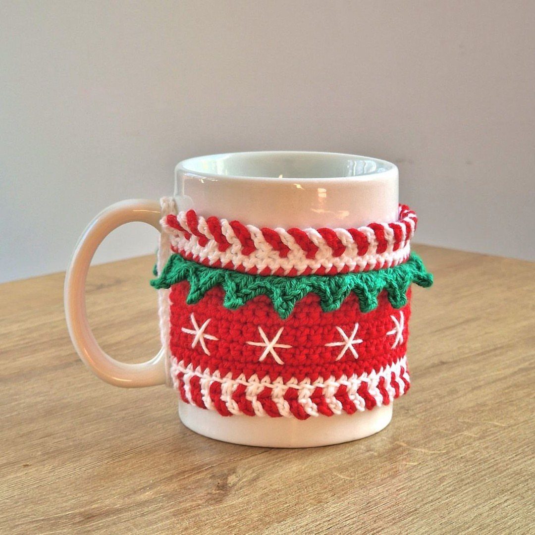 18 Christmas Gift Crochet Ideas for Everyone on Your List 4 A white ceramic mug featuring a red and green crocheted snowflake pattern cozy.