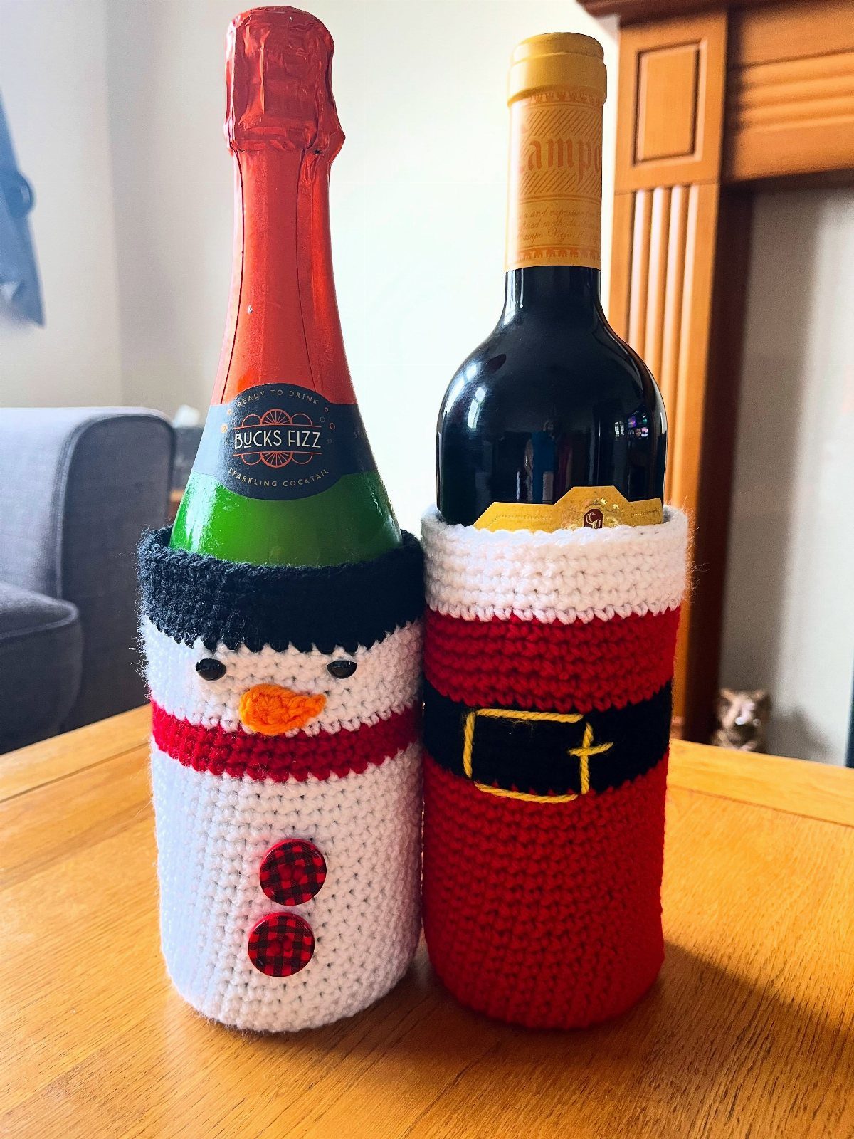 18 Christmas Gift Crochet Ideas for Everyone on Your List 7 Two wine bottles decorated with crochet cozies, one a snowman and one a red belt design.