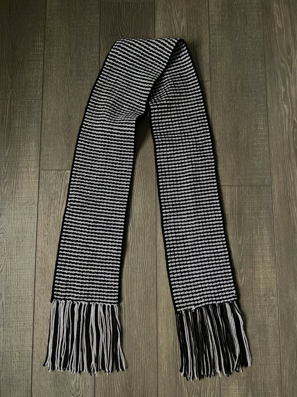 18 Christmas Gift Crochet Ideas for Everyone on Your List 16 A black and white striped crochet scarf with fringe lying on a wooden floor.