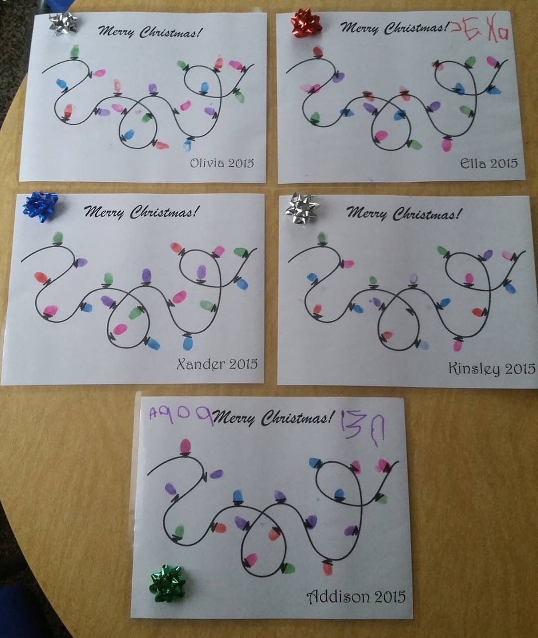 Five handmade Christmas cards featuring colorful fingerprint light designs and names.