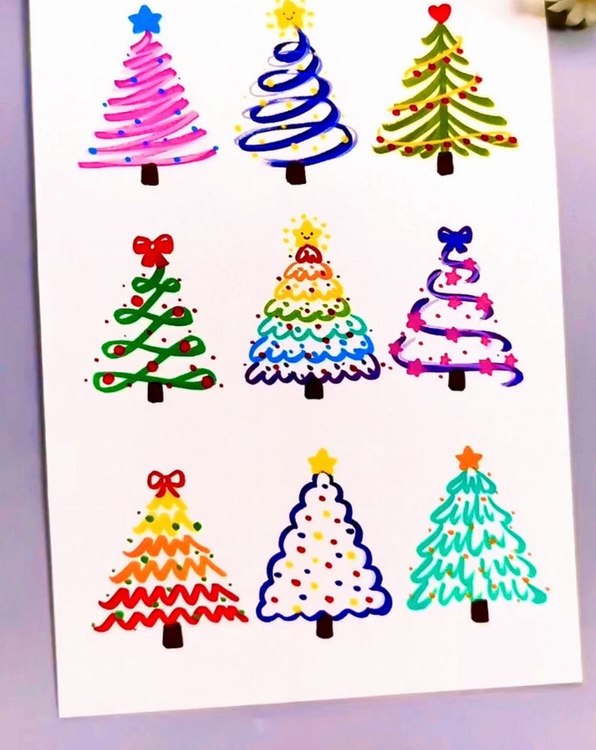 Nine colorful hand-drawn Christmas trees with different patterns on a white sheet of paper.