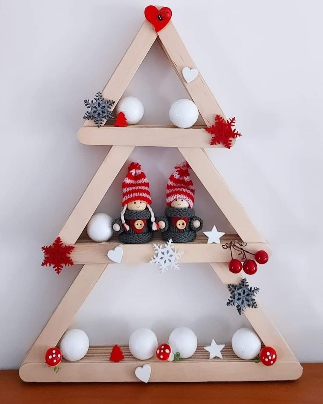A wooden shelf shaped like a Christmas tree decorated with small ornaments and gnome figurines.
