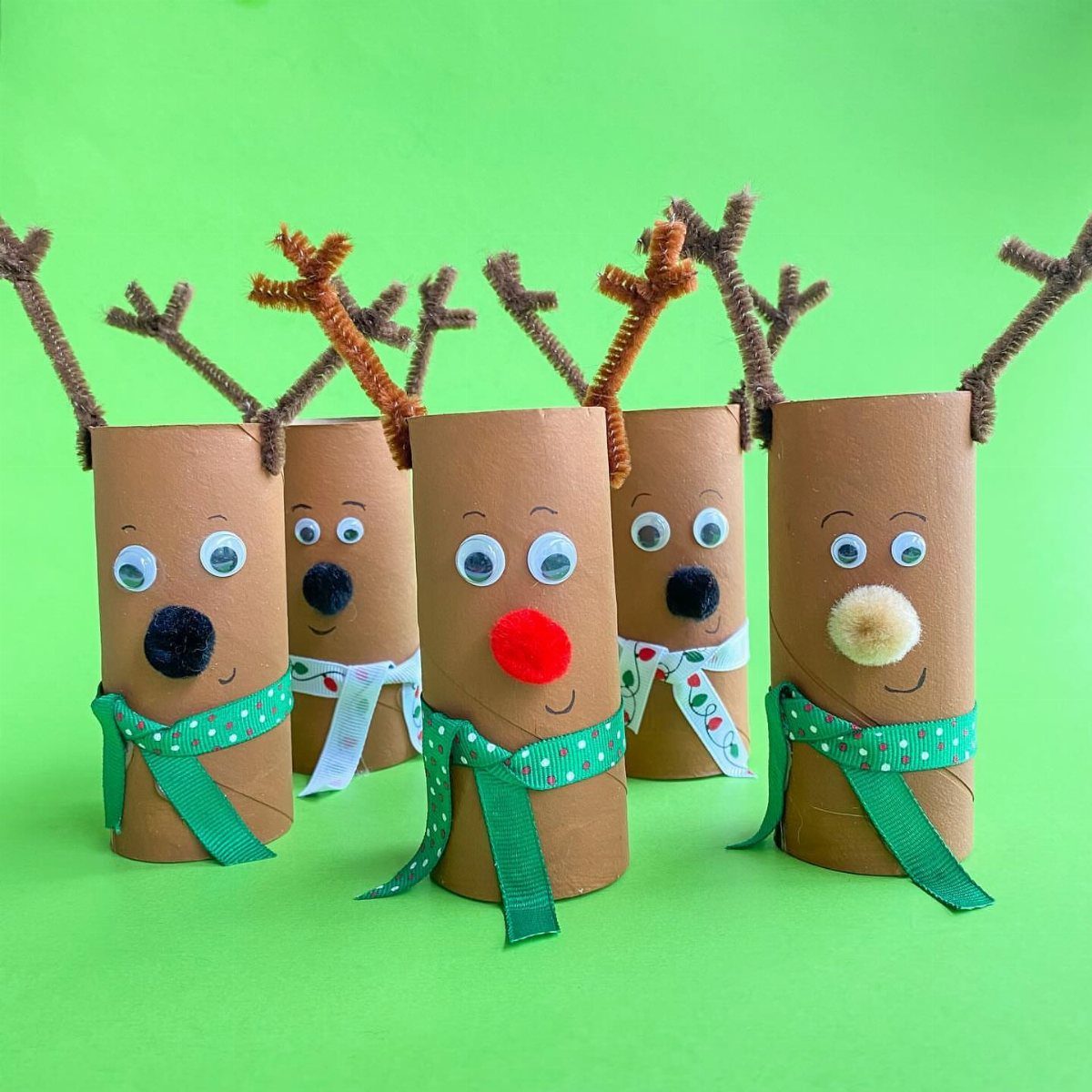 Five handmade reindeer crafts made from toilet paper rolls with pipe cleaner antlers and green scarves.