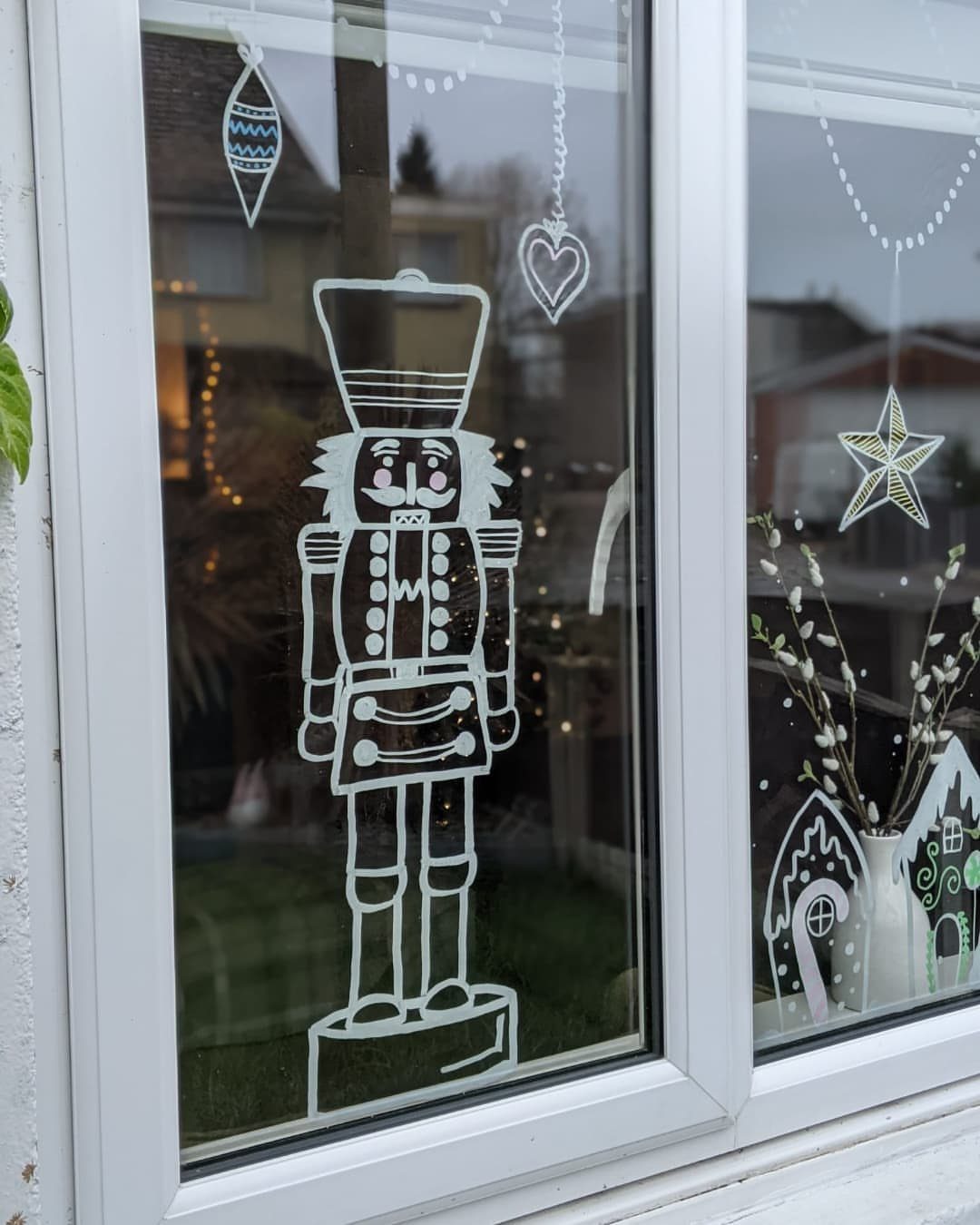 White nutcracker and ornament drawings on a glass window pane overlooking a residential area.