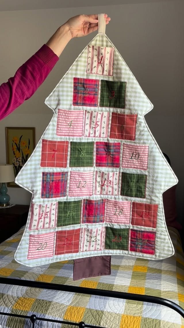 16 Christmas Sewing Projects That Cover the Whole Holiday 15 A person holding a tree-shaped fabric advent calendar with numbered colorful plaid pockets.