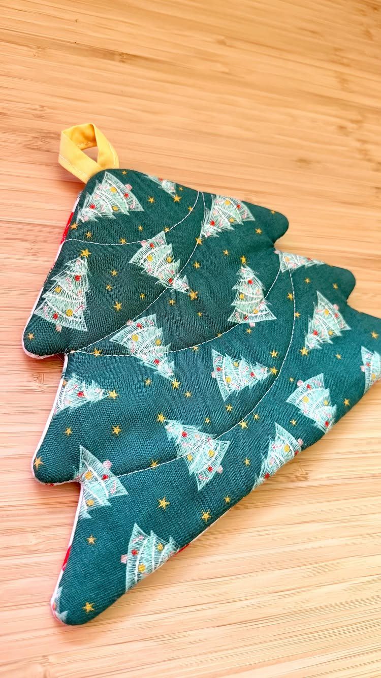 16 Christmas Sewing Projects That Cover the Whole Holiday 7 A green fabric Christmas tree shaped potholder resting on a wooden tabletop.