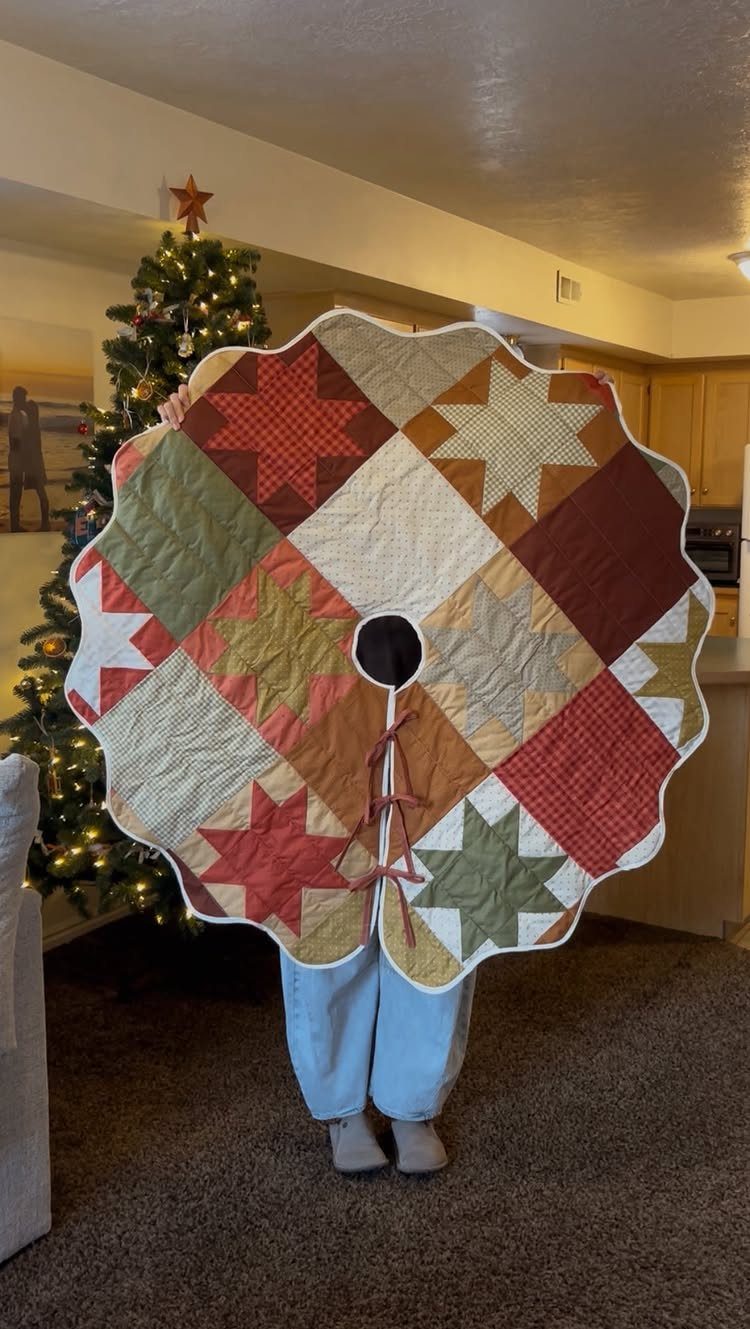 16 Christmas Sewing Projects That Cover the Whole Holiday 5 A person holding a large, circular, patchwork fabric Christmas tree skirt with star patterns.