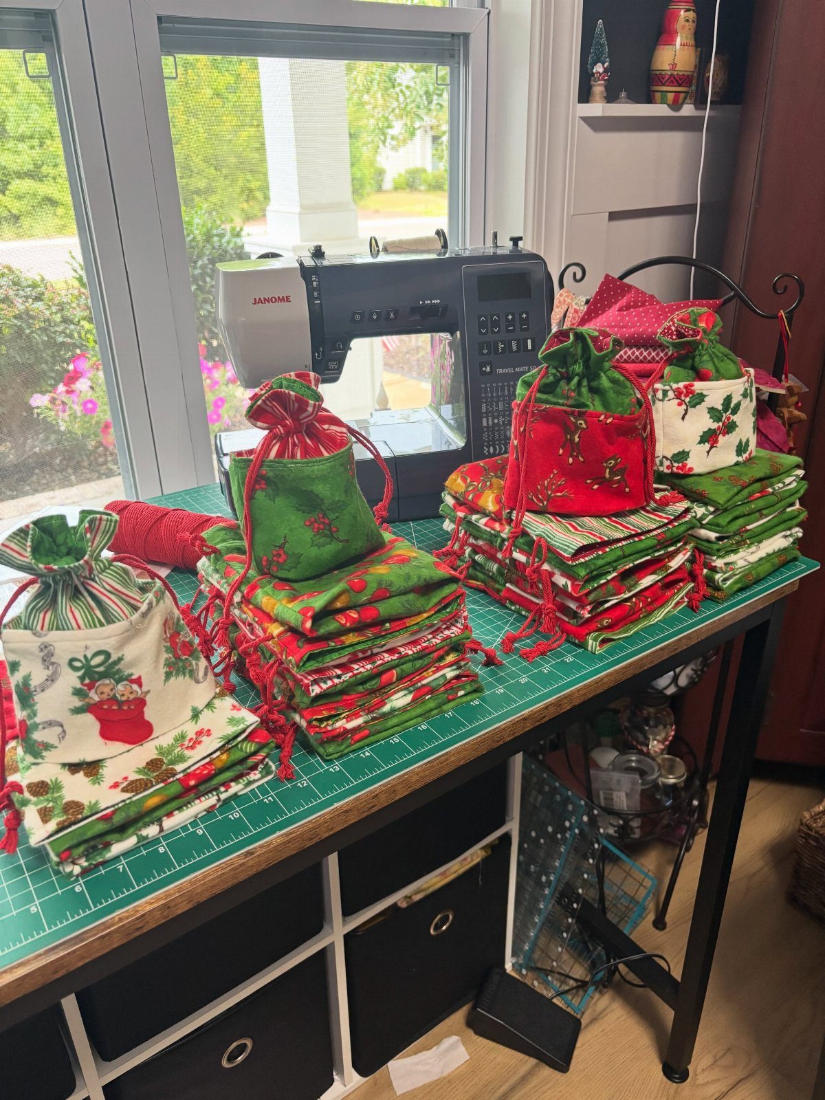 16 Christmas Sewing Projects That Cover the Whole Holiday 3 Small festive fabric drawstring gift bags stacked on a green cutting mat near a sewing machine.
