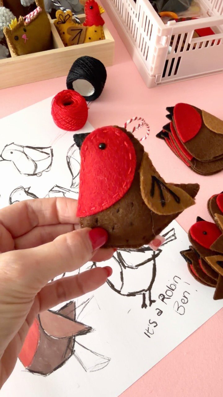 16 Christmas Sewing Projects That Cover the Whole Holiday 9 A hand holding a small red and brown felt bird ornament over sketches.