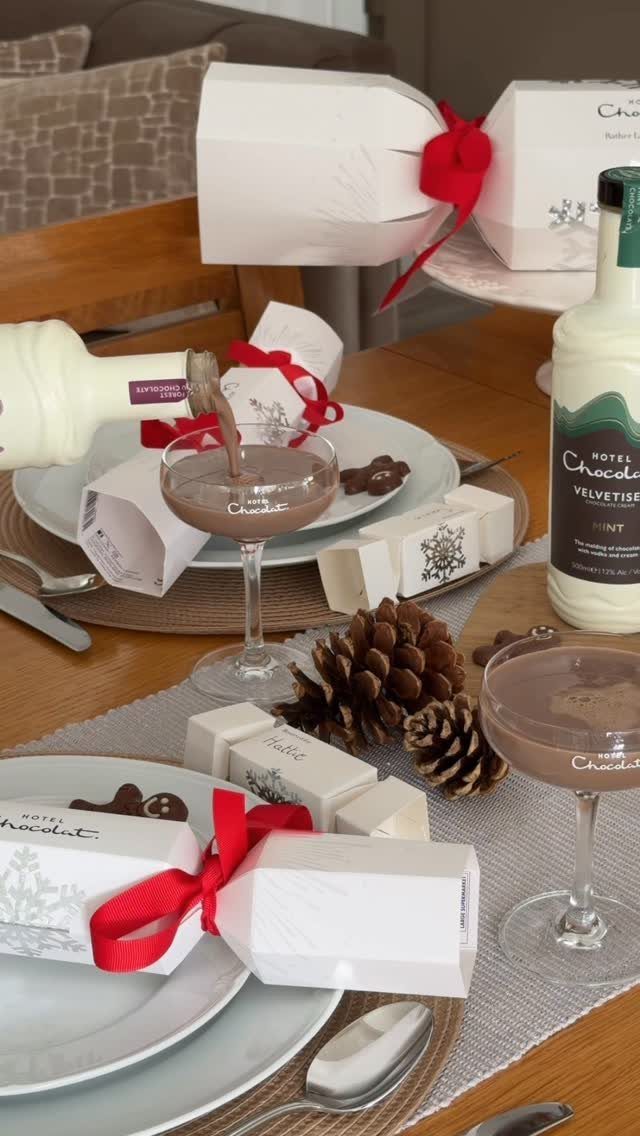 13 Christmas Table Decoration Ideas for Every Style 1 Festive table setting with white gift boxes, red ribbons, pinecones, and chocolate drinks in glasses.