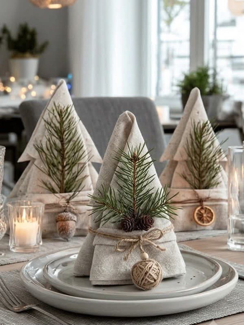 13 Christmas Table Decoration Ideas for Every Style 8 Folded linen napkins shaped like Christmas trees decorated with evergreen sprigs on white plates.
