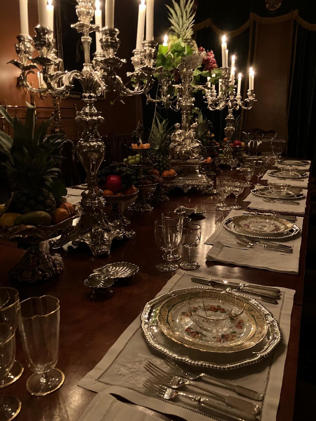 13 Christmas Table Decoration Ideas for Every Style 13 A formal dining table set with silver candelabras, ornate plates, and fruit centerpieces under warm lighting.