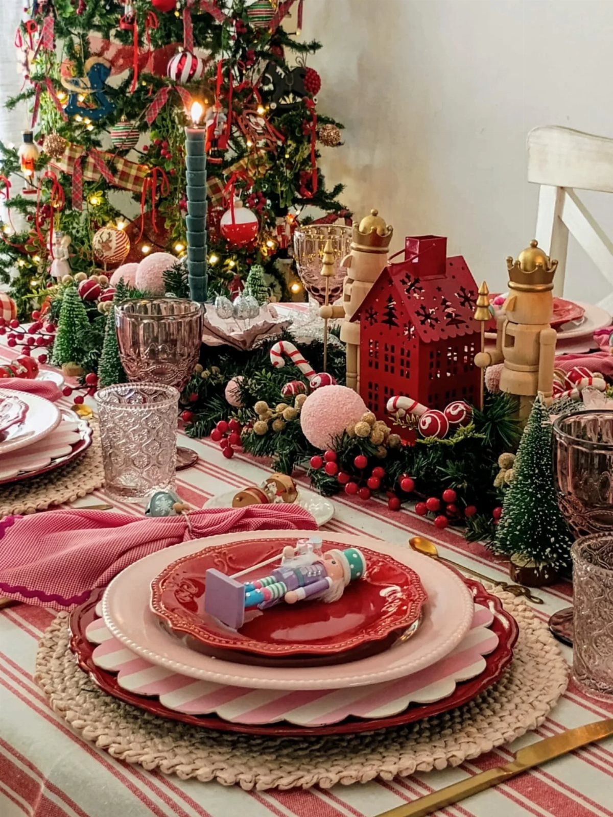 13 Christmas Table Decoration Ideas for Every Style 9 Christmas table decorated with nutcracker figurines, a red house, greenery, and pink themed tableware.