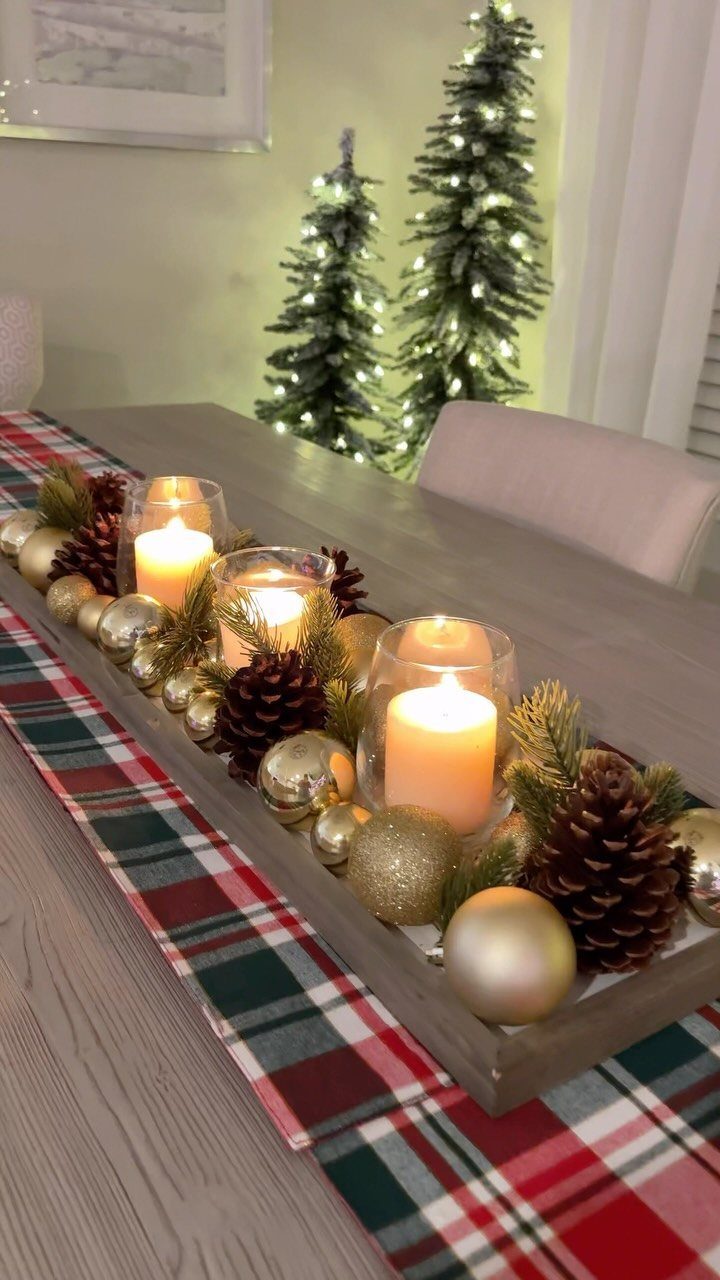 13 Christmas Table Decoration Ideas for Every Style 12 A wooden tray centerpiece with lit candles, pinecones, and gold ornaments on a plaid runner.