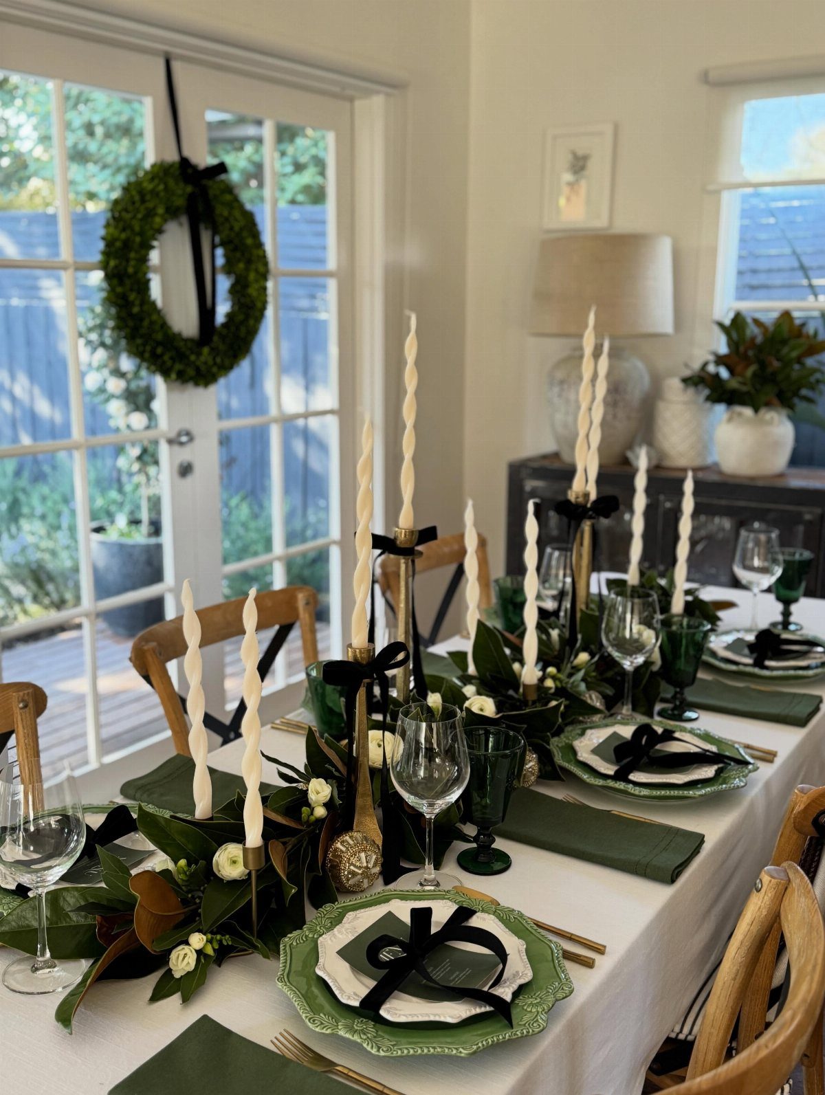 13 Christmas Table Decoration Ideas for Every Style 2 A festive dining table set with green napkins, gold cutlery, and a greenery centerpiece with tall candles.