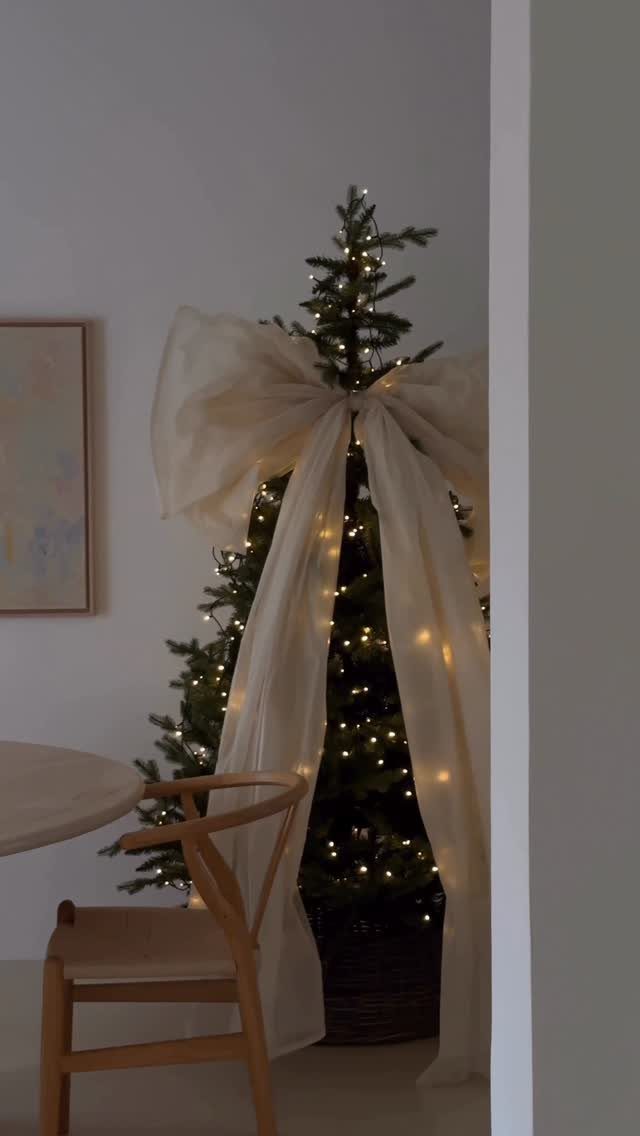 Christmas Tree Ribbon: 18 Styling Ideas That Work 11 A decorated Christmas tree featuring a large cream fabric bow and warm glowing fairy lights.