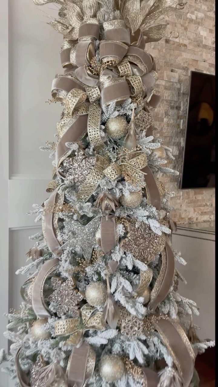 Christmas Tree Ribbon: 18 Styling Ideas That Work 13 Flocked Christmas tree decorated with champagne velvet ribbons and gold ornaments against a stone wall.