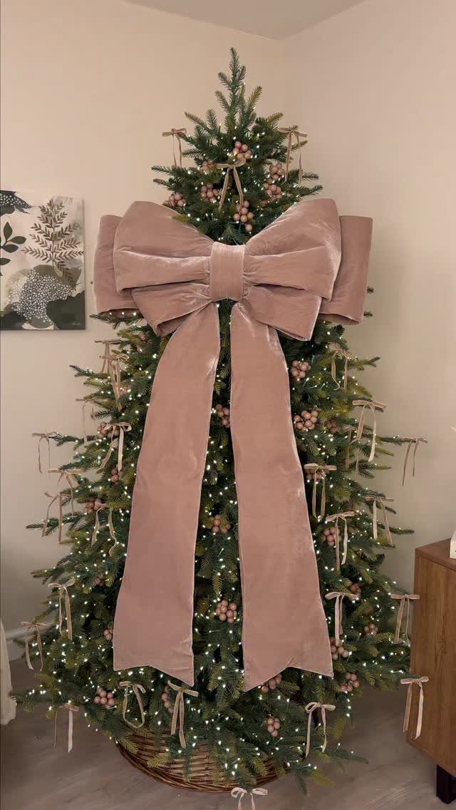 Christmas Tree Ribbon: 18 Styling Ideas That Work 17 Large dusty rose velvet bow acting as a topper on a lit Christmas tree.