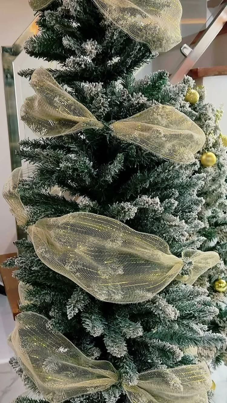 Christmas Tree Ribbon: 18 Styling Ideas That Work 6 Large gold mesh bows decorating a frosted green Christmas tree with snowy branches.