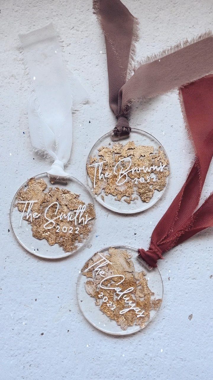 Cricut Christmas Balls: 14 DIY Ornaments for 2026 13 Three clear acrylic ornaments with gold flakes and white family names resting on a white surface.